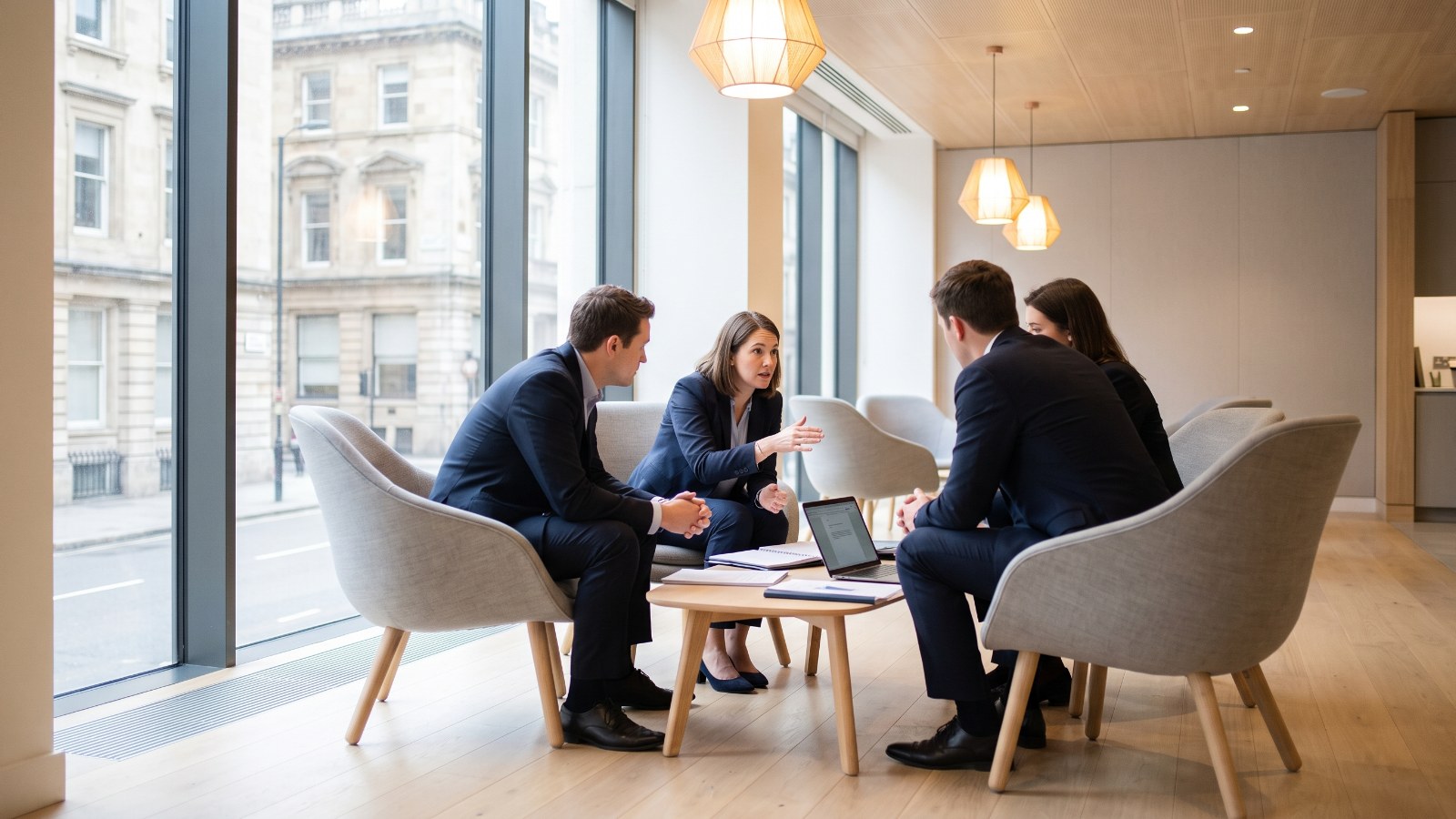 Four consultants in a working session around a low table, City street beyond the window